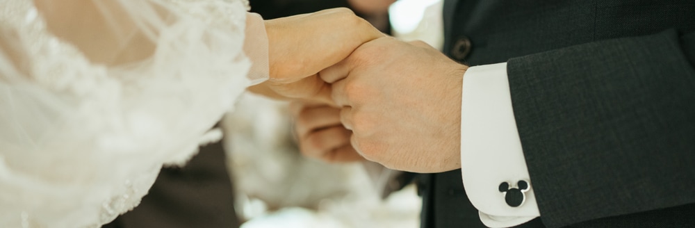 A bride and a groom who is wearing Mickey Mouse shaped cuff links holdings hands