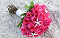 A bridal bouquet of roses and starfish lying on sand