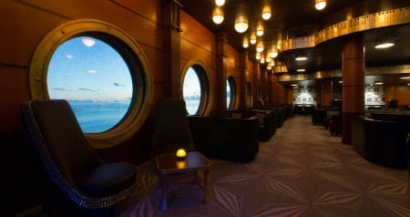 Tables next to a row of porthole windows at Keys, a piano bar on the Disney Magic.