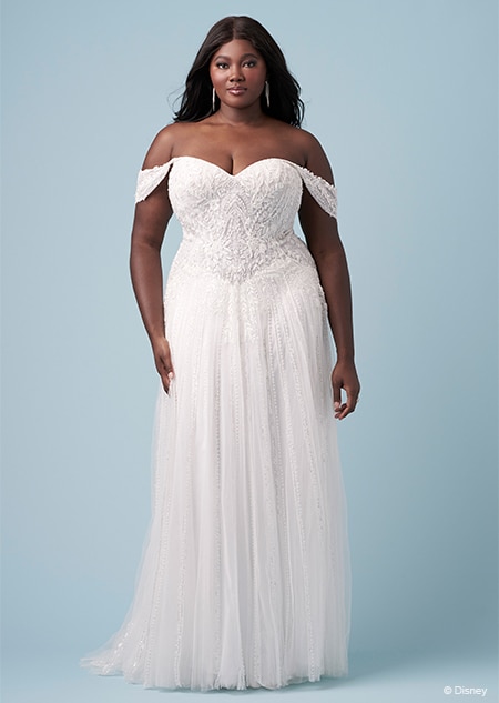 A bride wearing a Jasmine inspired sheath gown featuring off the shoulder sleeves, a sweetheart neckline and an embroidered bodice