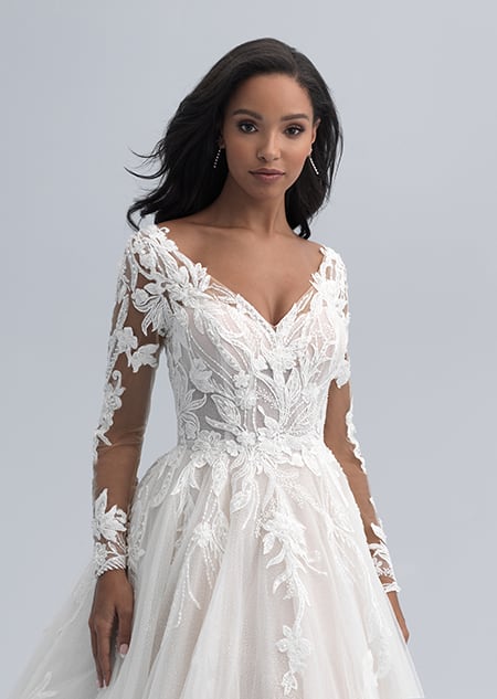 A bride wearing a wedding dress with long sleeves and large flowers and vines adorning the bodice