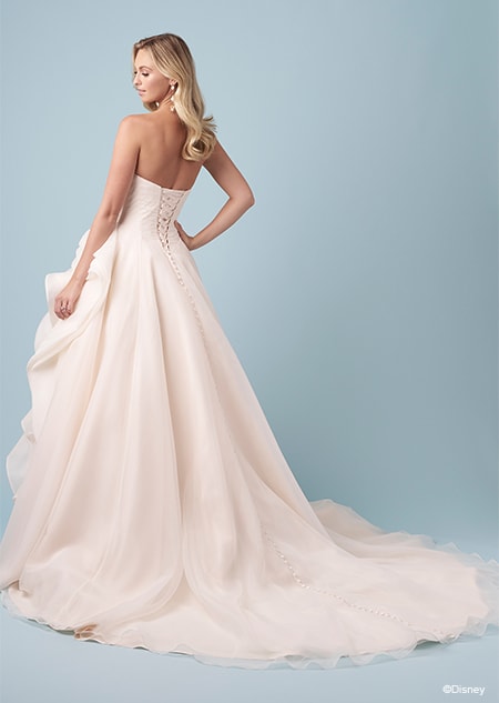 The back of a bride wearing a strapless Belle inspired A line wedding gown featuring a lace up back and a layered skirt gathered at the hip