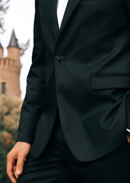 The midsection of a man wearing a black tuxedo jacket fastened with a Mickey Mouse shaped button