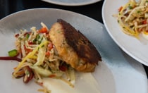 A plated dinner with crab cakes, vegetables, shredded cabbage and sauce