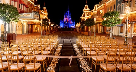 An evening wedding setup with rows of chairs and flower petals lining the aisle leading to Cinderella Castle