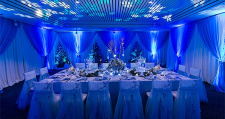 Indoor dining setup with elegantly draped chairs, a decorated table and winter themed decor 