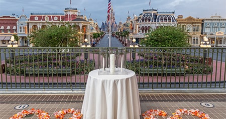 An outdoor wedding ceremony venue on a train station platform with arranged flower petals and a table with candles, overlooking Main Street, USA and Cinderella Castle