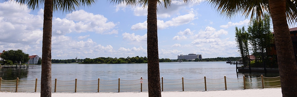 Palm trees, a sandy beach and a post and rope fence run along the edge of the Seven Seas Lagoon at Disney's Polynesian Village Resort