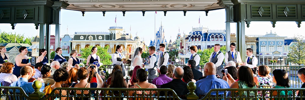 A bride and groom get married in front of a crowd of people in the train station overlooking Cinderella Castle