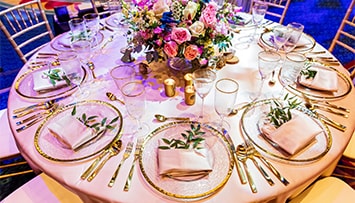 A circular table with a large floral center piece and 10 ornate place settings