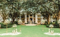 A stately manor with oak trees and a fountain is set up for an outdoor wedding on the lawn