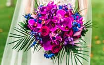 A bride holding a customized tropical bridal bouquet with palm fronds, orchids and roses