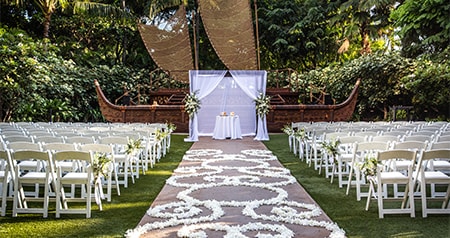 Rows of chairs along an aisle covered with flower petals leading to a table in front of a stage