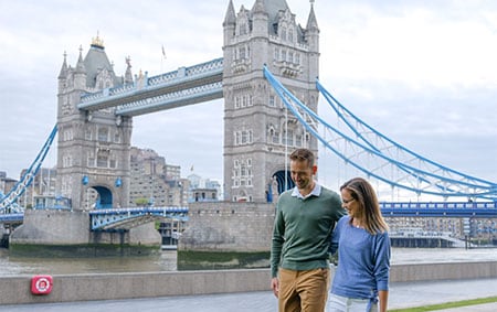 A couple with their arms around one another in front of the Tower Bridge in London, England