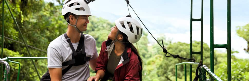 Newlyweds wearing zip line equipment on a platform in a rainforest in Costa Rica