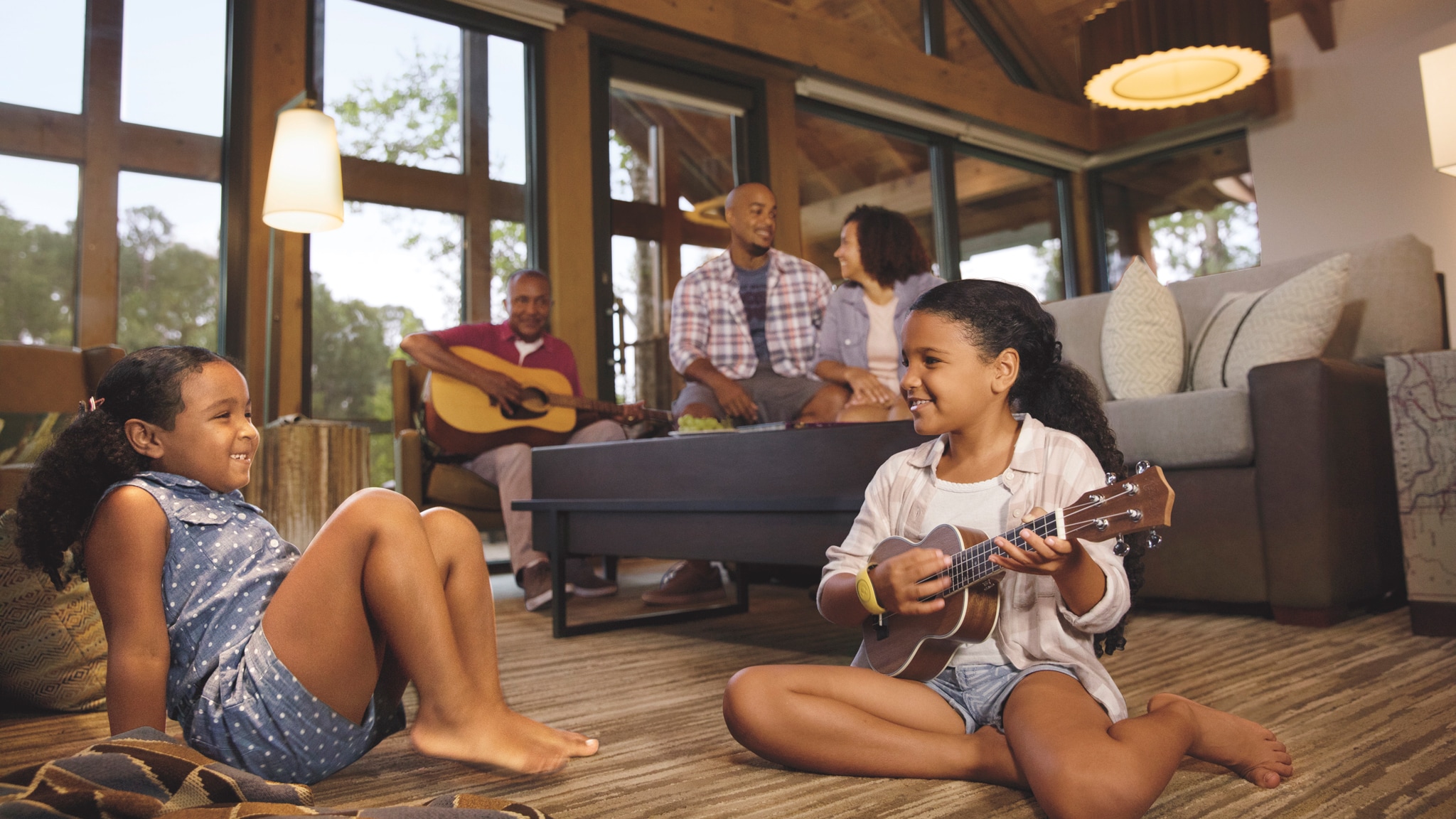 A young girl plays a small guitar while sitting on the floor of her cabin, as her parents relax on the couch behind her