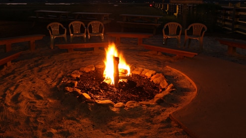 A campfire glowing in the dark and 5 empty chairs positioned to observe it