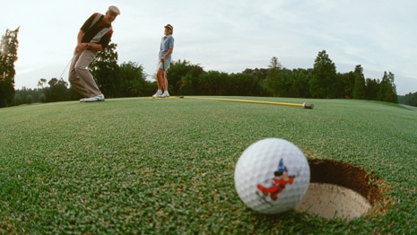 A golfer watches with his wife as the golf ball he putted perches at the edge of a hole
