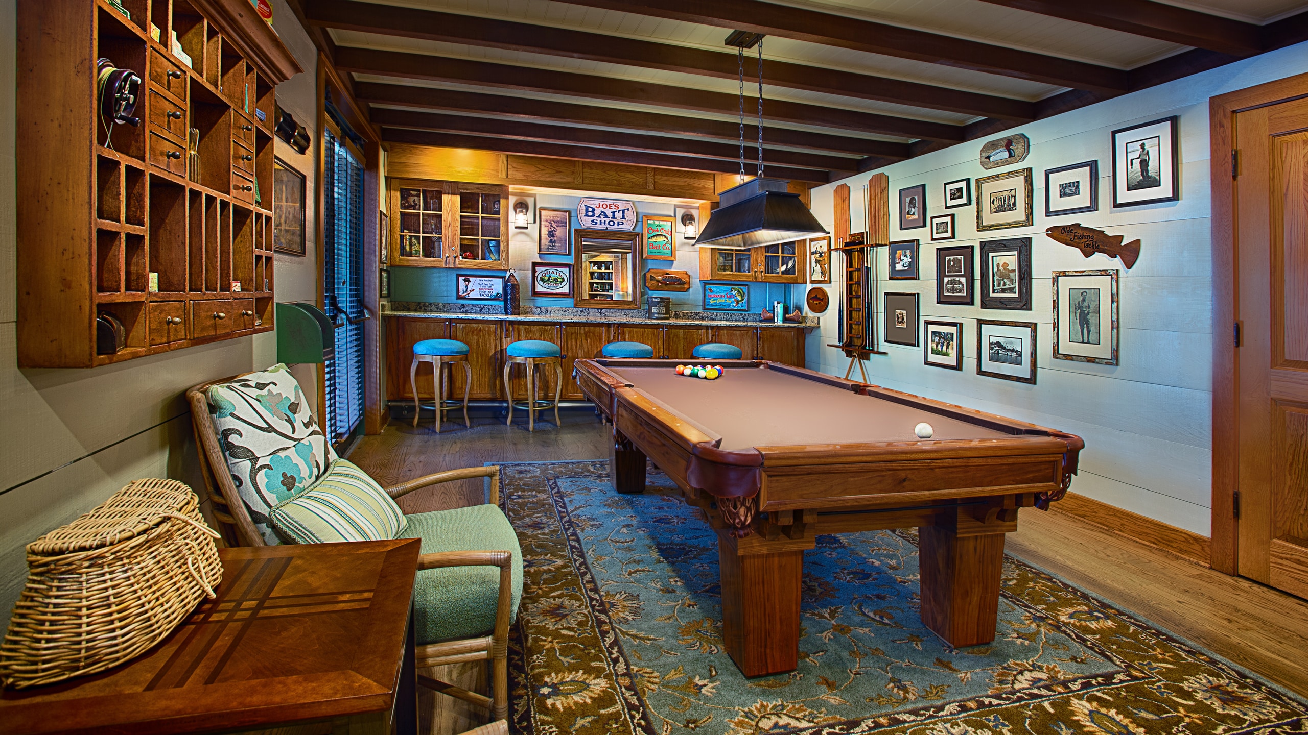 A pool table in a lodge with armchairs by a fireplace and bookshelves