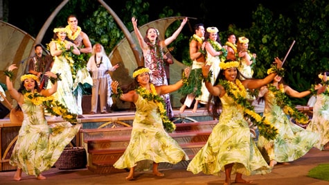 Dancers and singers on a stage, wearing Hawaiian dresses and floral leis