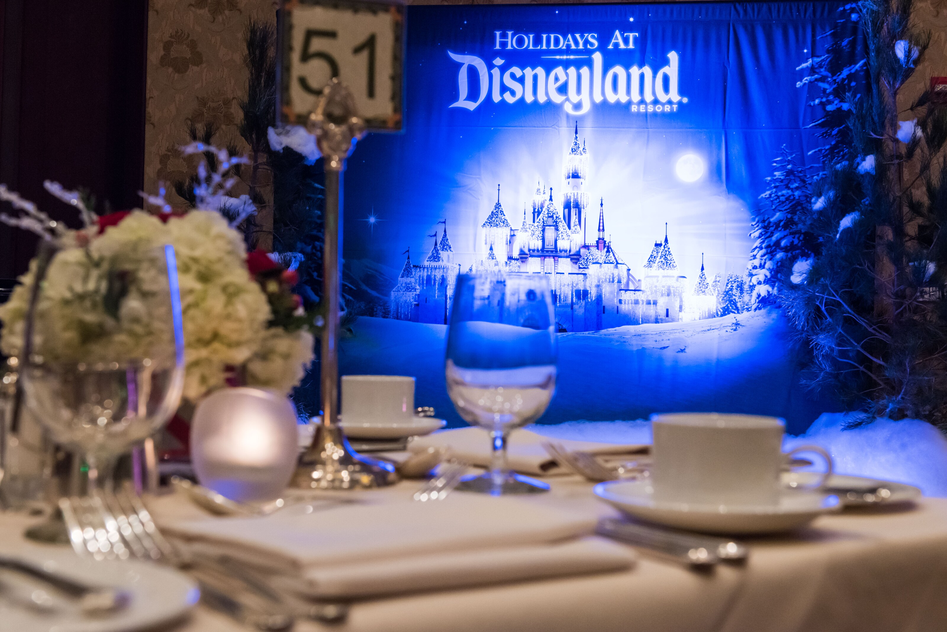 A holiday themed table setting beside a photo backdrop that reads Holidays at Disneyland Resort A holiday themed table setting beside a photo backdrop that reads Holidays at Disneyland Resort