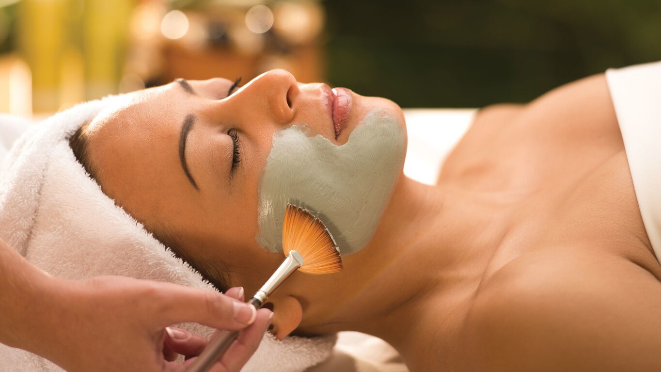 A woman with a towel on her head and her eyes closed relaxes during a facial