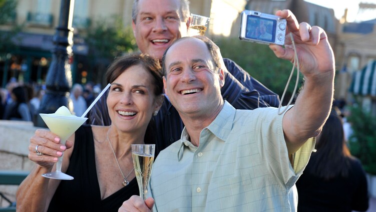 A woman with 2 men raising their beverages while taking a selfie