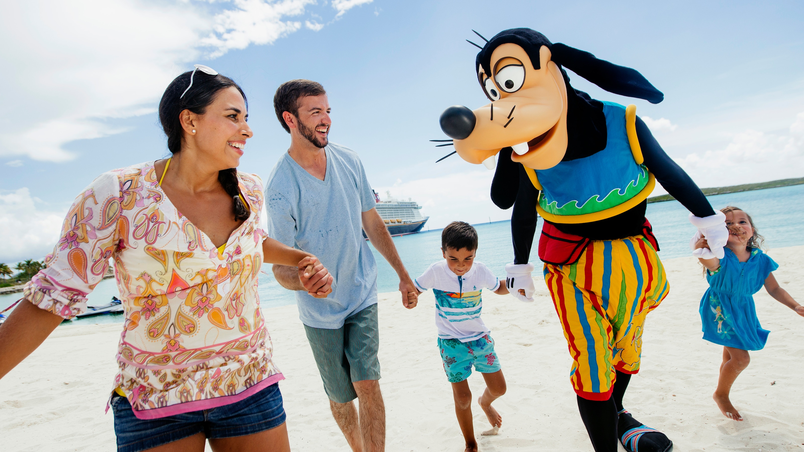 A man, woman, their son and daughter running along a beach with Goofy