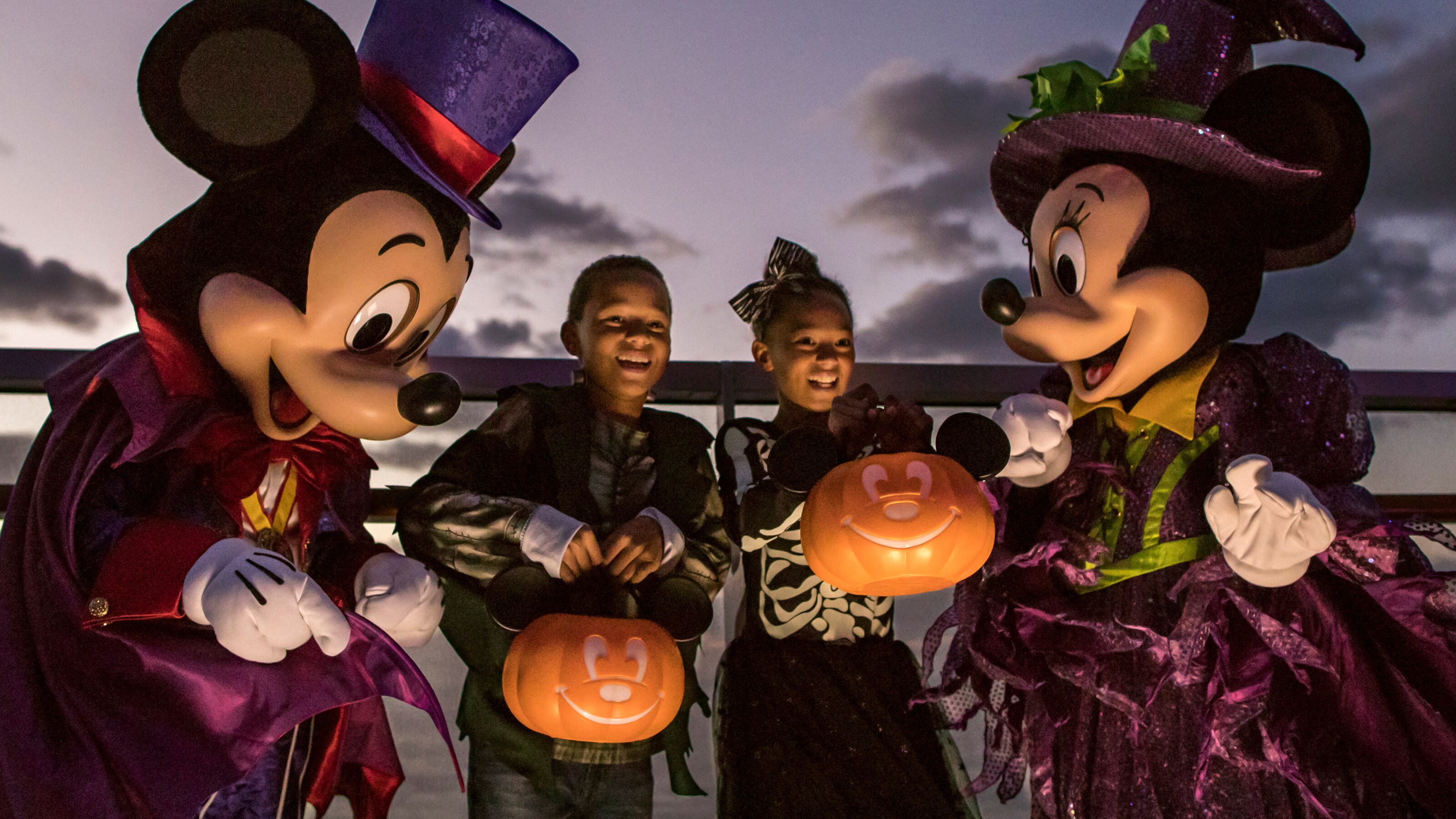Mickey and Minnie Mouse dressed in a Halloween costumes while standing with 2 kids