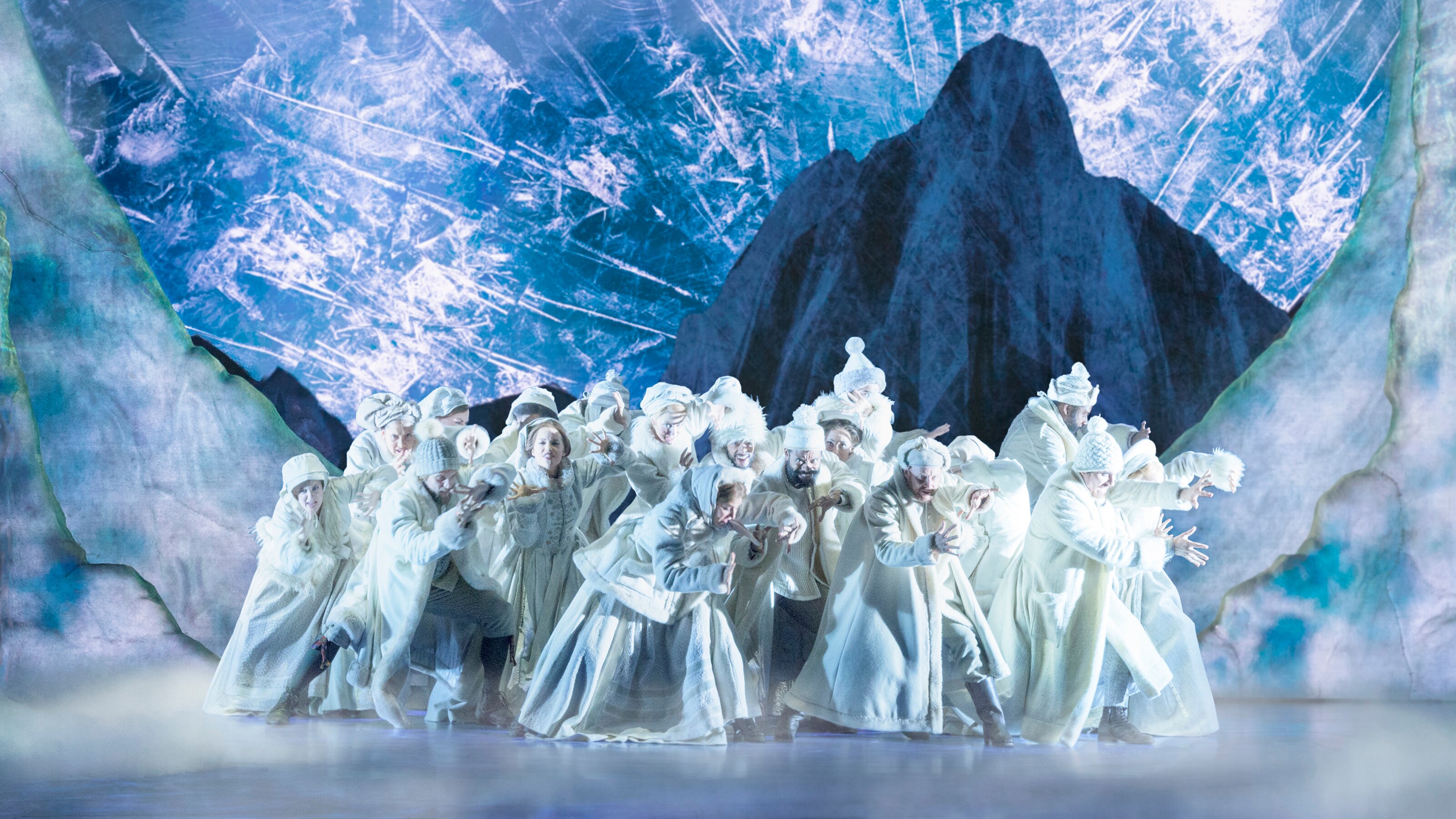 A group of actors wear long, hooded winter coats on the icy set of Frozen