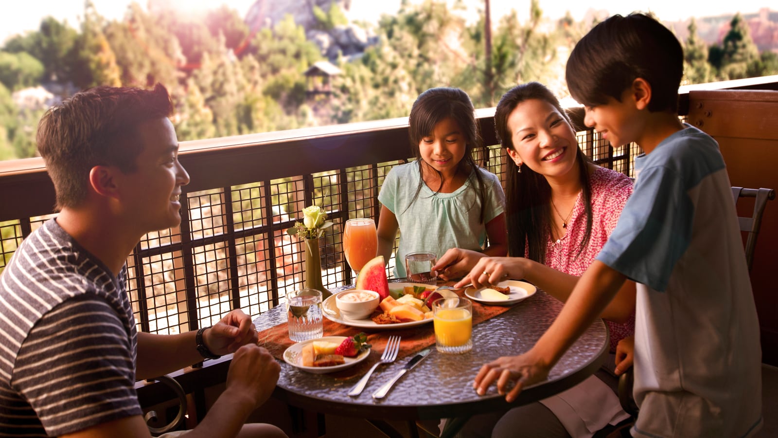 A family of 4 gather around a table with breakfast food on an outdoor balcony