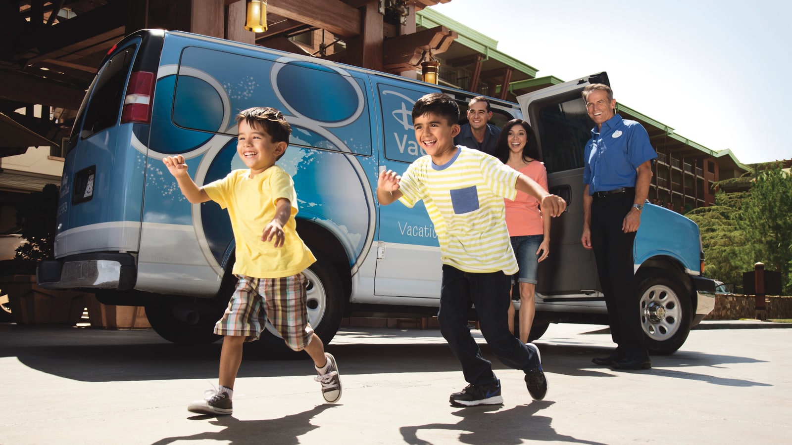 2 boys, a man and woman exit from a Disney Vacation Club van in front of a hotel