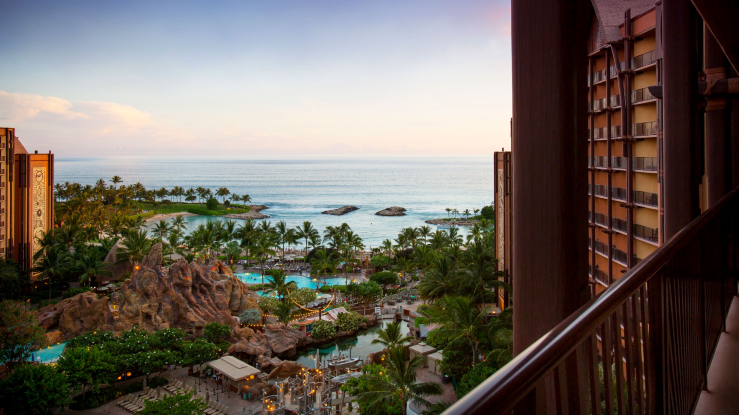 A balcony view of a tropical resort with pools and deck chairs, a blue lagoon and palm trees