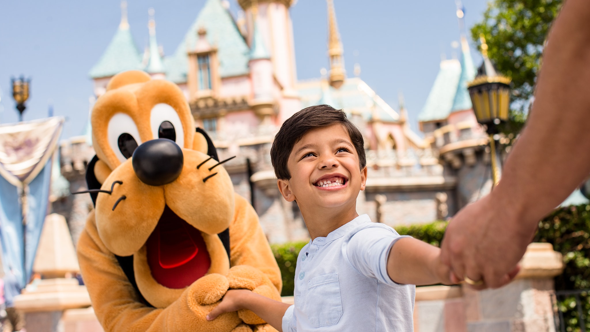 A young boy with 2 missing front teeth smiles as he holds hands with Pluto