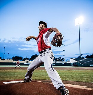 Under the stadium lights, a pitcher stands on the mound and prepares to throw a ball as his teammates get ready in the infield