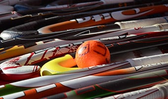 A field hockey ball sits on the ground among several field hockey sticks