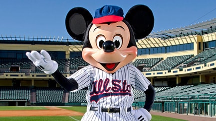 Mickey Mouse vestido con uniforme de béisbol parado en uno de los campos de béisbol