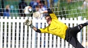 A goal keeper goes vertical to stop a shot on goal during a soccer match