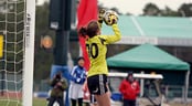 A female goal keeper stops a shot on goal during a soccer match