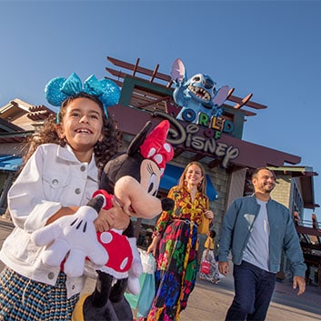 A girl holding a Minnie Mouse plush with her parents in front of World of Disney at Disney Springs