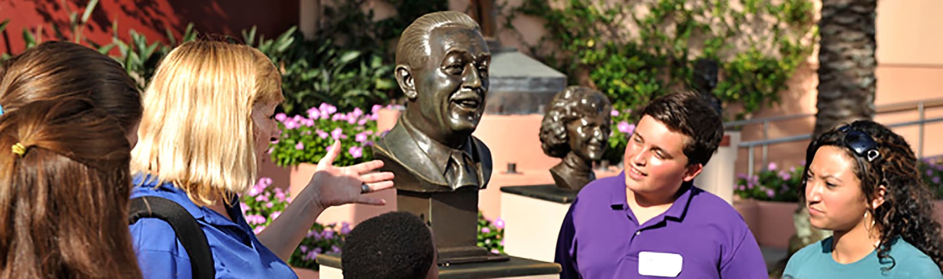 Children watching a Cast Member gesturing towards a bust of Walt Disney
