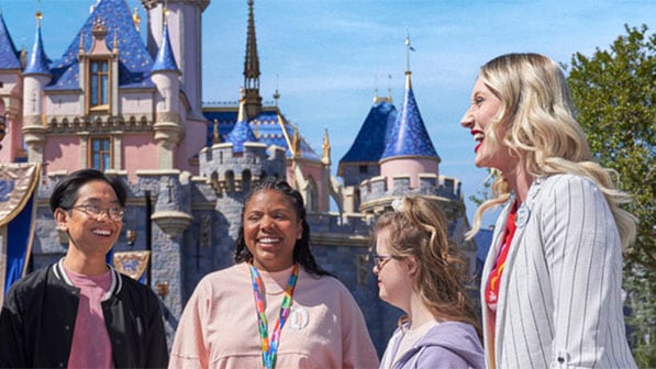 A Cast Member and 3 students stand in front of Sleeping Beauty Castle in Disneyland Park