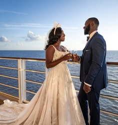 A bride and groom holding champagne glasses while standing on the upper deck of a Disney cruise ship