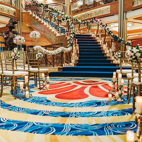 A Disney Cruise Line ship atrium with a staircase, decorated with flowers and candles for a wedding ceremony